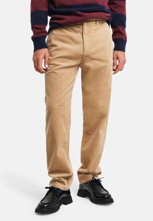 Pantalons en velours côtelé beige avec une coupe droite et une légère texture. Portés avec des chaussures noires à lacets et un pull rayé bleu marine.