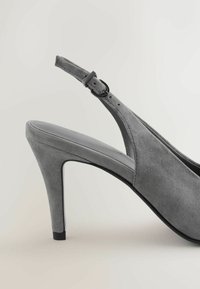 Szürke velúr slingback cipő, hegyes orral és vékony, magas sarkával. A pánt állítható csattal rendelkezik a megfelelő illeszkedés érdekében.