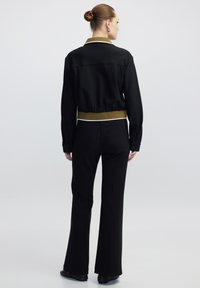 Zwarte jas met een cropped ontwerp en olijfgroene kraag, gecombineerd met zwarte flared broek. Kenmerken zijn zichtbare stiksels en een gladde textuur.