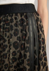 Fascia elastica nera con logo "JOOP!", gonna in rete con stampa leopardata in toni terrosi, caratterizzata da nastro nero con dettagli del logo.