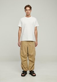Hvid bomulds-T-shirt, løse beige bomuldsbukser og sorte sandaler. Enkelt design, blød tekstur og afslappet pasform.