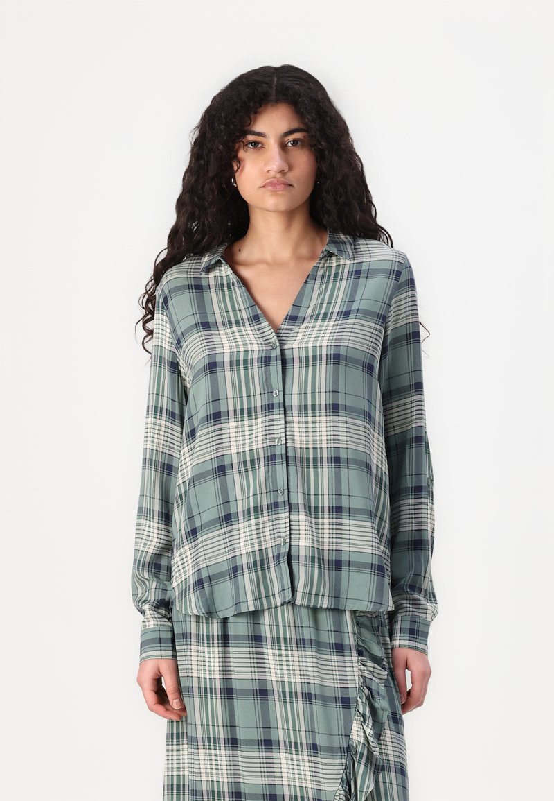 Green plaid button-up shirt with long sleeves, featuring white and navy stripes. Made from a smooth fabric with a relaxed fit.