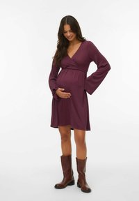 Oblačilo za materinstvo v temno vijolični tkanini, z dolgimi zvončastimi rokavi in imperijskim pasom. Ujemajoč s svetlosrnimi škornji do kolen.