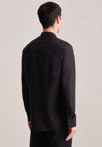 Črna majica z dolgimi rokavi slim fit kroja, s pritisnimi manšetami in zaobljenim robom. Gladka tekstura tkanine z rahlim sijajem.