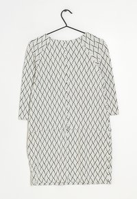 Černobíle vzorovaný oděv s herringbone designem, kulatým výstřihem a rukávy třičtvrtě délky, visící na há čku.