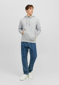 Gray hooded sweatshirt with long sleeves, featuring a front pocket and drawstrings. Paired with light blue relaxed-fit jeans and white shoes.