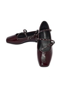 Ballerines en cuir verni bordeaux avec un bout carré, dotées de brides entrecroisées ornées de clous en argent. Texture lisse et talon bas.