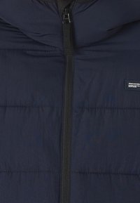 Marineblå dunjakke med fuld lynlås, quiltet design og et Abercrombie-mærke på venstre side. Glat, holdbart stof.