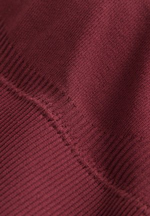 Close-up of burgundy knit fabric showing detailed stitching and texture with ribbed and smooth sections.