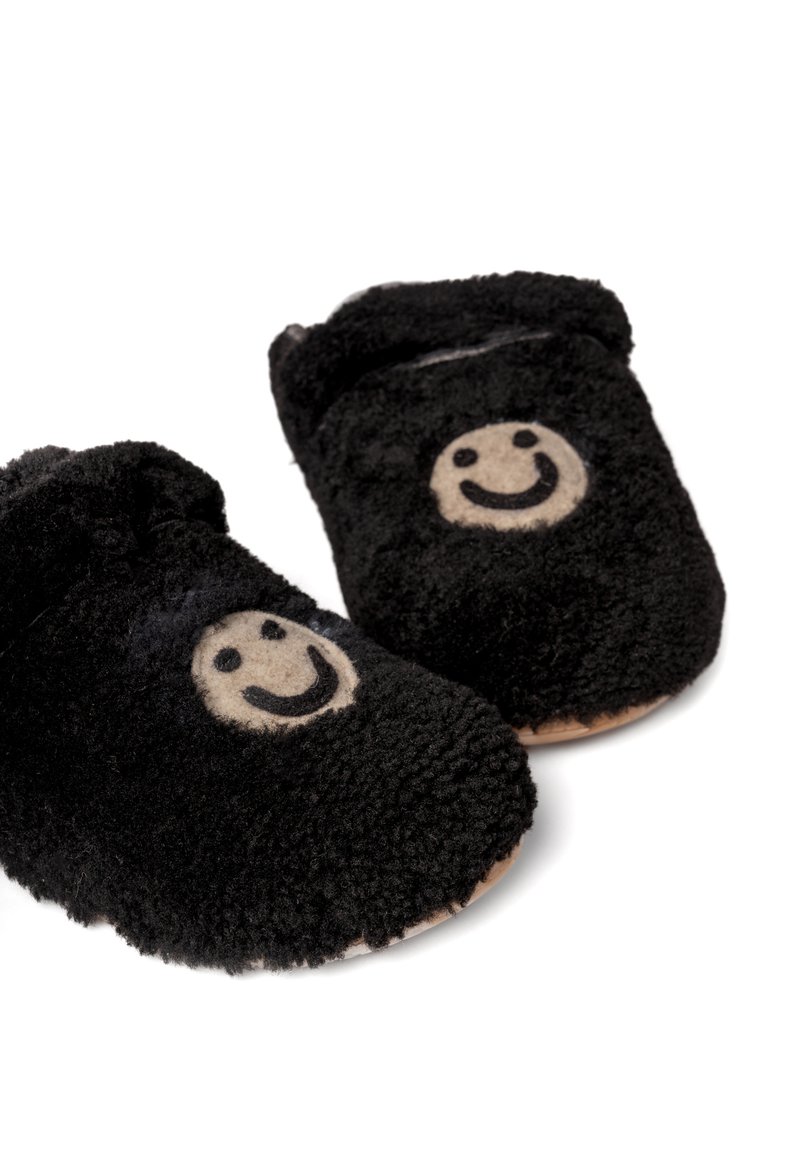 Czarne pluszowe kapcie o miękkiej, puszystej fakturze, z beżowym wzorem uśmiechniętej buźki z przodu i brązową podeszwą.