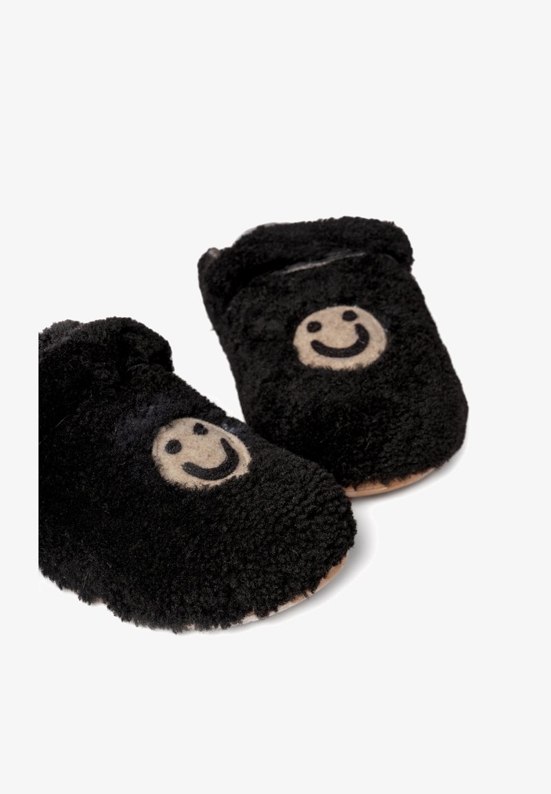 Czarne pluszowe kapcie o miękkiej, puszystej fakturze, z beżowym wzorem uśmiechniętej buźki z przodu i brązową podeszwą.