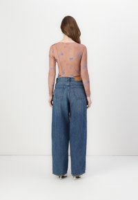 Langermet, gjennomskinnelig topp i dempet ferskenfarge med blå mønstre, kombinert med høyhalset, løs blå denimjeans som har to baklommer.