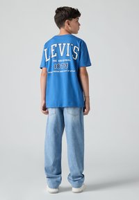 Camiseta de algodón azul con el logo "LEVI'S" en blanco, jeans de pierna ancha en azul vaquero y zapatillas blancas con suelas texturizadas.