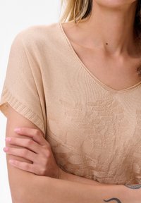 Beige gebreid top met een v-hals, korte mouwen en een textuur van bladeren. Glad stoffen met een zachte glans, aangevuld met ribbelaccenten.