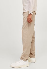 Beige bomullsbukser med en avslappnad passform, med sidokanter och bärs med vita sneakers. Skjortan har lätt tyg och knappdetaljer.