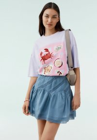 Lila oversized t-shirt met een krabgrafiek op een roze achtergrond; gecombineerd met een blauwe gelaagde rok met een gestructureerd patroon en kantafwerking.