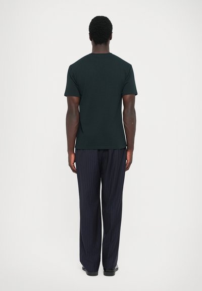 Melna kokvilnas T-kreklā ar īsām piedurknēm un apaļu kakla izgriezumu, apvienota ar jūraszils svītrainām biksēm, skatīta no aizmugures.