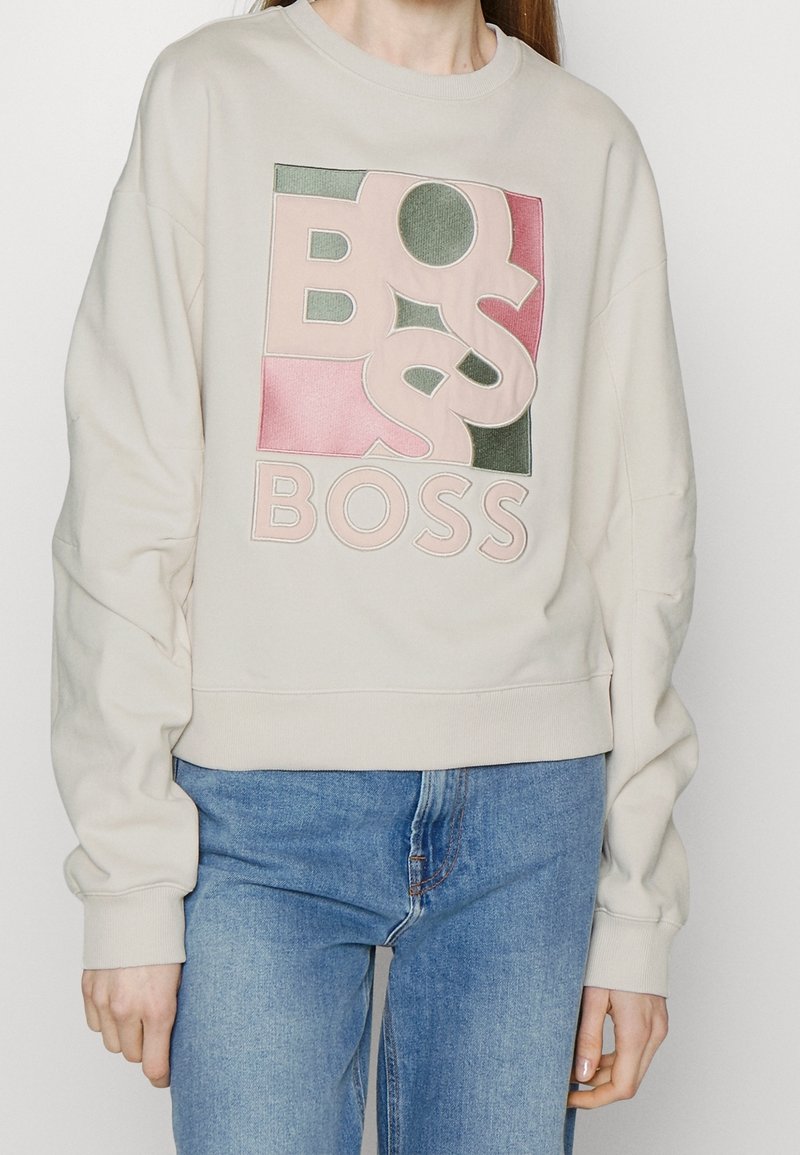 Felpa beige in cotone con un grande logo "BOSS" multicolore sul davanti. Vestibilità comoda con polsini e orlo a costine.