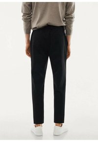 Pantaloni neri a gamba dritta, con una texture liscia, vita elastica e tasche posteriori discrete, abbinati a sneakers bianche.