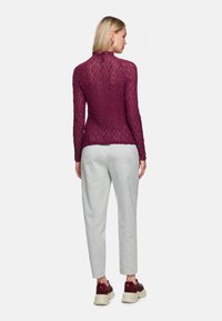 Weinrotes, strukturiertes Langarmoberteil mit figurbetonter Form und hohem Kragen, kombiniert mit hellgrauen, zulaufenden Hosen und burgunderroten Sneakern mit klobigen Sohlen.