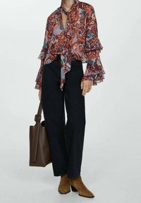 Blouse fleurie à manches volantées en rouge, bleu et violet ; associée à un jean noir taille haute et des bottines en daim marron.