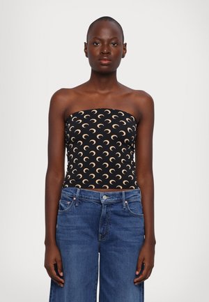 Schwarzes trägerloses Oberteil mit einem Muster aus Halbmonde in Beige; hat ein figurbetontes Design. Kombiniert mit blauen weit geschnittenen Jeans.