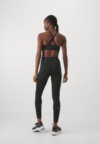 Black athletic crop top with crossed straps, paired with high-waisted black leggings featuring reflective accents and textured panel details.
