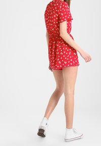 Mono corto de manga corta rojo con patrón floral blanco, cintura ceñida y dobladillo con volantes. Combinado con zapatillas altas blancas.