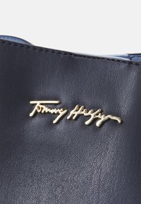 Granatowa torebka z ekoskóry z złotym logo Tommy Hilfiger, teksturowana powierzchnia i kontrastowe niebieskie wnętrze.