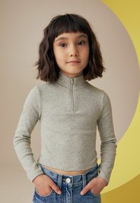 Lys grå, ribbet langærmet top med en halv-zip krave, kombineret med høj-taljede blå denimshorts. Enkel, tætsiddende design.