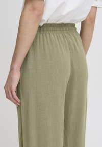 Pantalons amples vert olive avec une taille élastique, en tissu léger texturé et avec des poches latérales, vus de dos.