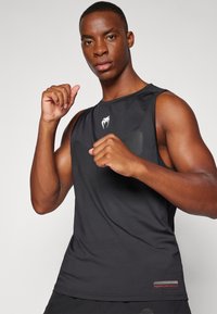 Top sportivo nero con scollo rotondo, pannelli testurizzati sul petto e accento rosso "PERFORMANCE" vicino all'orlo.