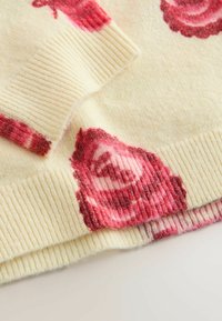 Gestrickter Pullover in Creme mit rosa Blumenmuster. Mit gerippten Bündchen und Saum. Weiche Textur mit leichtem Glanz, der die Blumenmuster hervorhebt.