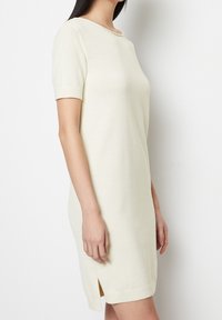 Abito a maglia a maniche corte di colore crema chiaro, con scollatura tonda e spacco laterale, realizzato in un tessuto texturizzato e dalla vestibilità comoda.