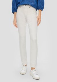 Jasnobeżowe skinny jeans o gładkiej fakturze, pięciokieszoniowym stylu i metalowym zapięciu. Zestawione z białymi trampkami dla casualowego wyglądu.