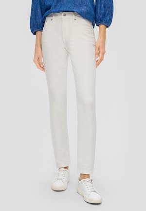 Jean skinny beige clair avec une texture lisse, design à cinq poches et fermeture à bouton en métal. Associé à des baskets blanches pour un look décontracté.