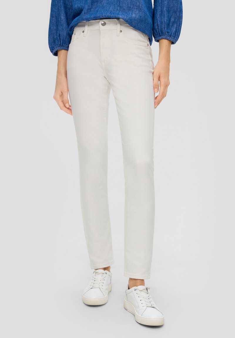 Jasnobeżowe skinny jeans o gładkiej fakturze, pięciokieszoniowym stylu i metalowym zapięciu. Zestawione z białymi trampkami dla casualowego wyglądu.