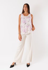 Top senza maniche floreale con motivi viola e verdi, abbinato a pantaloni ampi bianchi e scarpe nere con tacco alto. Tessuto con una consistenza liscia.