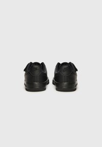Sorte Nike-sneakers med en glatt skinnfinish, rund tå og bakre trekkstropper. Sålen er teksturert med et flatt design.