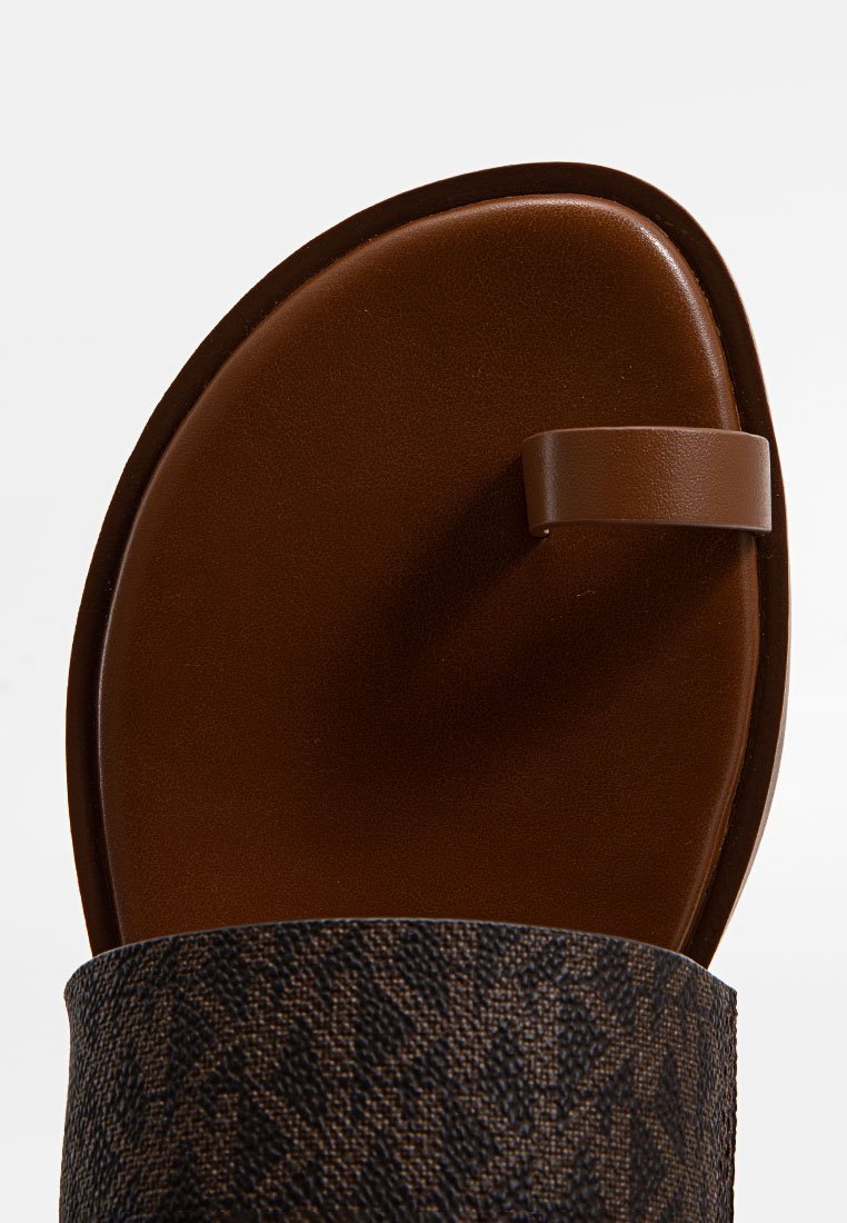 Sandale marron avec une sangle en tissu texturé, semelle lisse et un design minimaliste. Présente un entre-doigt étroit pour plus de stabilité.