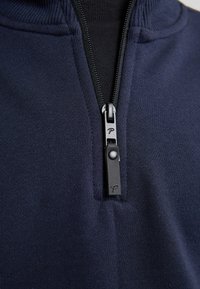 Pullover navy in tessuto testurizzato con zip liscia e linguetta, caratterizzato da un logo; colletto alto con bordi a coste.