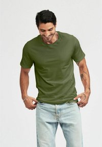 Grön bomullströja med korta ärmar och rund hals, kombinerad med blekta blå jeans. Har en avslappnad passform och mjuk textur.