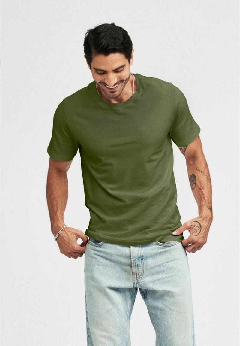 Grön bomullströja med korta ärmar och rund hals, kombinerad med blekta blå jeans. Har en avslappnad passform och mjuk textur.