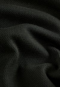 Tessuto nero con una superficie liscia e morbida, caratterizzato da un sottile motivo a costine e una leggera lucentezza, drappeggiato e leggermente stropicciato.