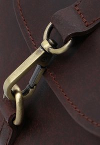 Matériau en cuir marron avec une texture usée. Quincaillerie en bronze, comprenant une boucle et un détail de couture. Focalisation sur la boucle de fixation et la sangle.