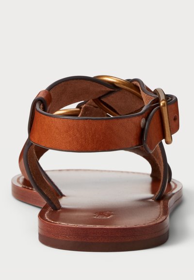 Brūnas ādas sandales ar jostu dizainu, zelta detaļām, atvērtu aizmuguri un platu zoli. Gluda tekstūra un noapaļoti stūri.