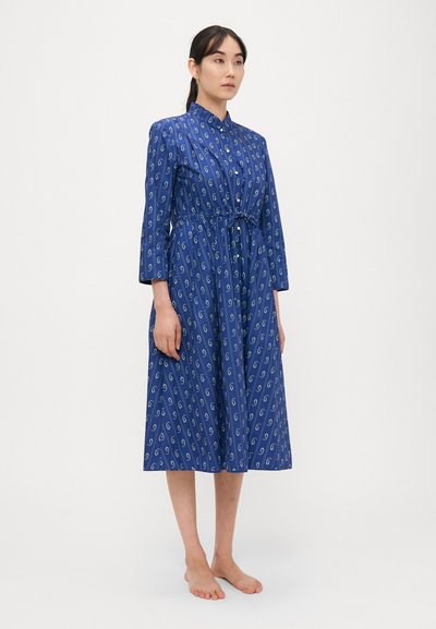 Μακρύ μπλε φόρεμα με γιακά που κουμπώνει, διακοσμημένο με άσπρα και πράσινα αφηρημένα σχήματα, με δέσιμο στη μέση και μανίκια τριών τετάρτων.