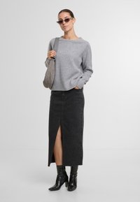 Grau gestrickter Pullover mit geripptem Saum, schwarze Jeans-Midi-Rock mit Schlitz vorne und kniehohen schwarzen Lederstiefeln. Accessoire: graue Umhängetasche.