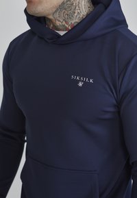 Navy hooded sweatshirt made of smooth fabric, featuring a front pocket and a small white "SIKSILK" logo on the chest.