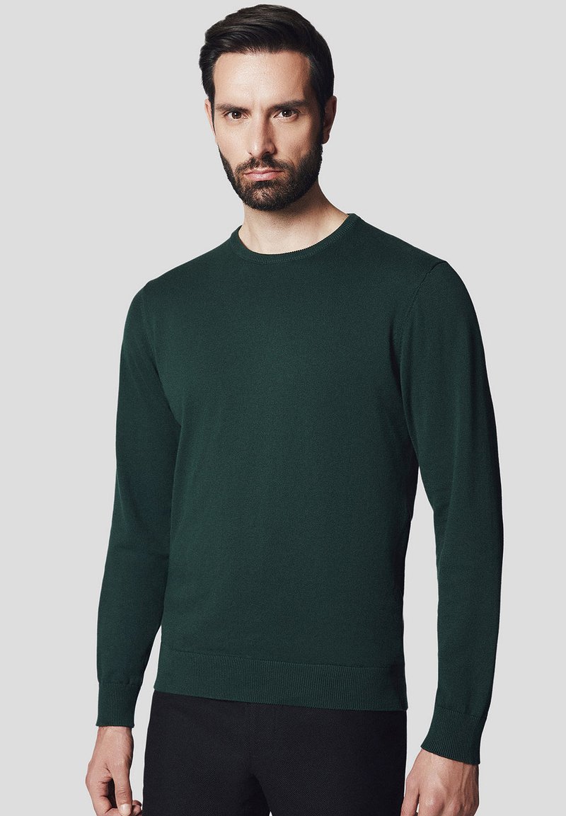 Ciemnozielony sweter z dzianiny, z okrągłym dekoltem i długimi rękawami. Posiada prążkowane mankiety i dół, gładką teksturę oraz dopasowany krój.